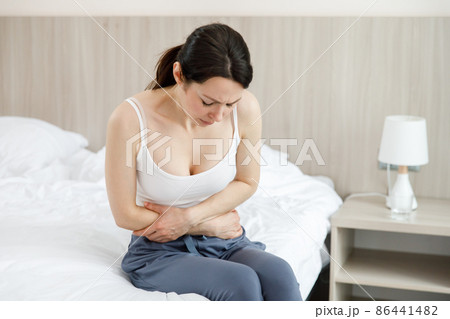 Cystitis in a woman. A young woman has a pain in the lower abdomen, she holds her stomach with her hand. Cystitis in a woman. A young woman has a pain in the lower abdomen, she holds her stomach with her hand. 86441482
