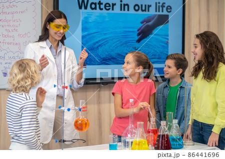 Telling teacher and attentive children standing near table Telling teacher and attentive children standing near table 86441696