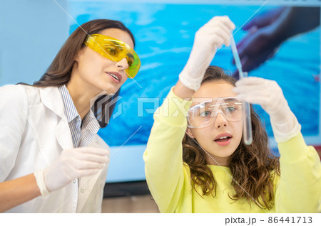Girl with pipette over test tube and observing teacher Girl with pipette over test tube and observing teacher 86441713