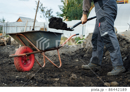 Working with garden tools, shovel and wheelbarrow on the site of a country house. Preparation for construction work. 86442189