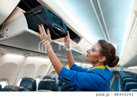 Stewardess putting travel suitcase in overhead luggage bin in aircraft Stewardess putting travel suitcase in overhead luggage bin in aircraft 86443241