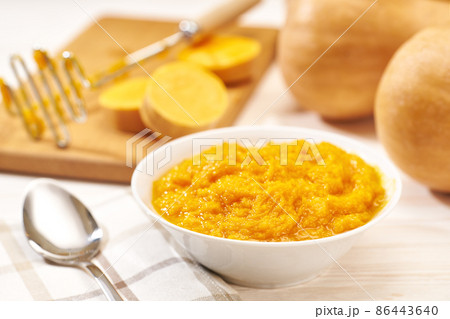 Pumpkin puree in a ceramic bowl, fresh pumpkin, squash, butternut close up on white kitchen table. 86443640