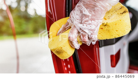 Young woman cleaning part of car door, closeup detail on hand in glove holding yellow sponge 86445069