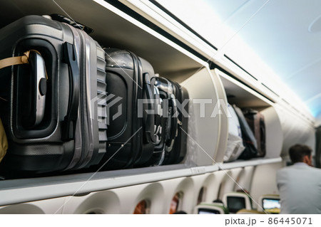 Airplane overhead locker with black plastic baggage suitcases, closeup detail Airplane overhead locker with black plastic baggage suitcases, closeup detail 86445071