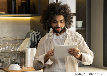 Young Egyptian man orders food via tablet in home kitchen 86445673