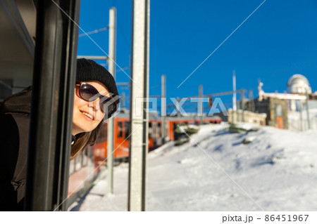 Happy woman in sunglasses sticking head out of train window passing among snowy areas 86451967