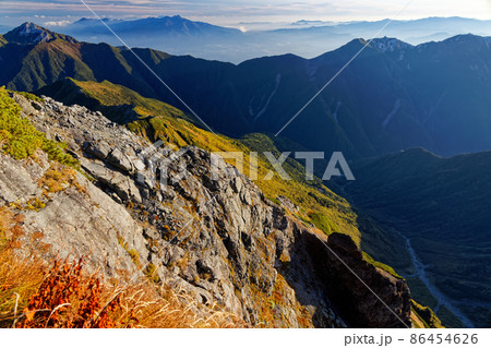 南アルプス・北岳山頂から朝日を浴びるバットレスの岩壁と甲斐駒ヶ岳・八ヶ岳・鳳凰山の眺め 86454626