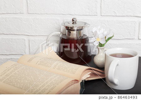 Morning tea. An open old book on the kitchen table and a cup of tea. Leisure reading in a cozy loft-style room 86463493