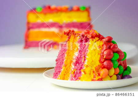 Rainbow celebration cake, coloured sponge cake filled and covered with frosting and hand decorated with chewy fruit candies in a crisp sugar shell with fruit flavour 86466351