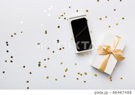 Opened gift box with gold ribbon and smartphone on color background, top view. Blank open box packaging mockup , Template for your design - branding mockup 86467488