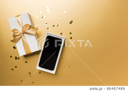 Opened gift box with gold ribbon and smartphone on color background, top view. Blank open box packaging mockup , Template for your design - branding mockup Opened gift box with gold ribbon and smartphone on color background, top view. Blank open box packaging mockup , Template for your design - branding mockup 86467489