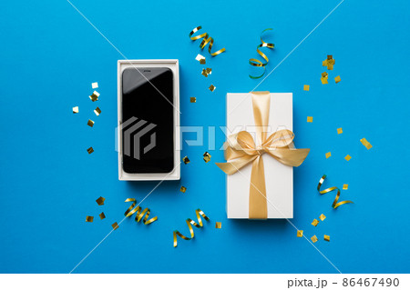 Opened gift box with gold ribbon and smartphone on color background, top view. Blank open box packaging mockup , Template for your design - branding mockup 86467490