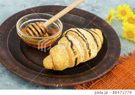 Fresh croissant, honey, yellow flowers. 86471779