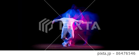 Dynamic portrait of male hip-hop dancer dancing isolated on dark background in mixed neon light. Youth culture, hip-hop, movement, style and fashion, action. Dynamic portrait of male hip-hop dancer dancing isolated on dark background in mixed neon light. Youth culture, hip-hop, movement, style and fashion, action. 86476546