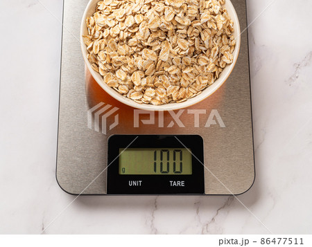 Raw dry oatmeal in a bowl on a digital kitchen scale.  86477511