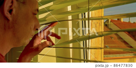 Midlle age man looking through a jalousie. Themes curiousity, surveillance or eyesight 86477830