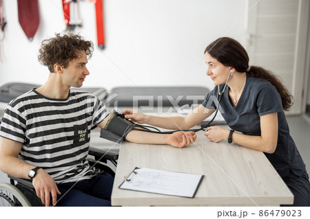 Medical worker measures the pressure of a young man in a wheelchair Medical worker measures the pressure of a young man in a wheelchair 86479023