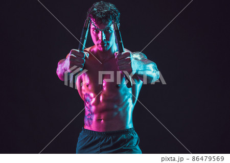 Portrait of strong man who holds nunchaku while isolated on black background. Sport concept 86479569