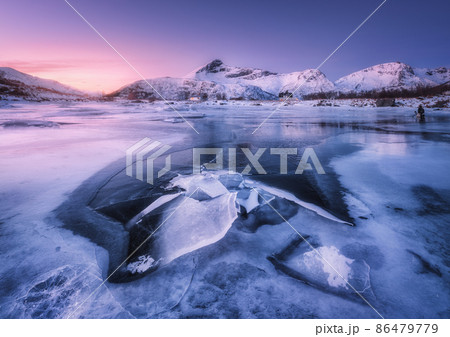 Snowy mountains, blue sea with frosty coast, reflection in water and purple sky at colorful sunset Snowy mountains, blue sea with frosty coast, reflection in water and purple sky at colorful sunset 86479779