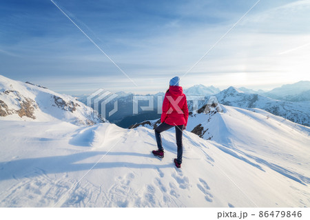 Young woman in red jacket in snowy mountains at sunset in winter 86479846