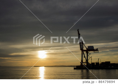 夕暮れの釧路港の岸壁でオレンジ色の夕陽を浴びて立っているコンテナ用クレーン 86479894
