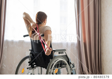 Caucasian woman in a wheelchair doing exercises with the help of fitness rubber bands.  86480379