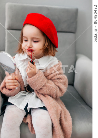 Red lipstick, bright baby lips. Fashionable child in a red beret and mother's shoes with heels. funny little girl making makeup with mother cosmetics 86480432