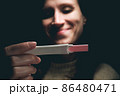 A woman in a dark room looks at the result of a pregnancy test and smiles. 86480471