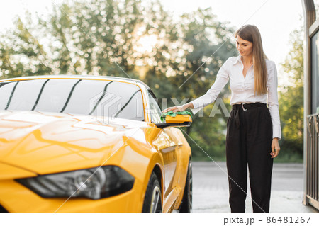 Young woman in business outfit, shirt and trousers cleaning rearview car mirror 86481267
