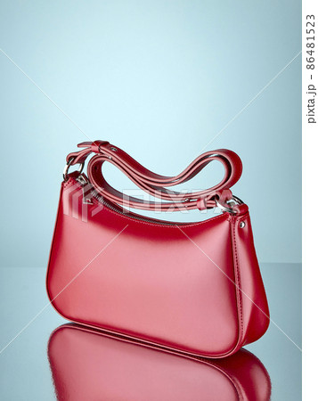 Fashionable handbag made of glossy red leather, standing on a mirror surface, on a pale blue background with a reflection. Copy space. 86481523