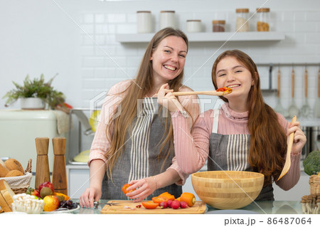 In a white, spotless modern kitchen, a smiling mother and daughter demonstrate how to prepare veggies for dinner. In a white, spotless modern kitchen, a smiling mother and daughter demonstrate how to prepare veggies for dinner. 86487064