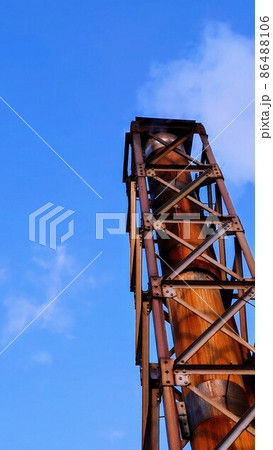 風呂屋の錆びた煙突が煙を吐く午後の青空 86488106
