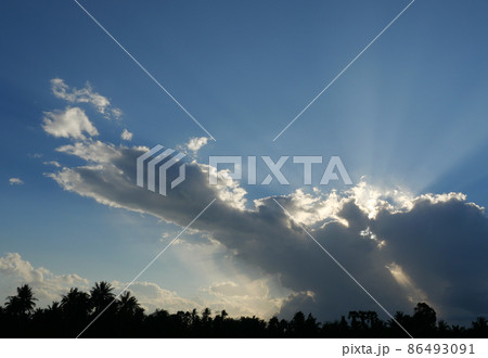 Cumulus cloud with sunbeam on beautiful blue sky , Silhouette of coconut palm tree with black color fluffy cloud at sunset at tropical zone , Thailand Cumulus cloud with sunbeam on beautiful blue sky , Silhouette of coconut palm tree with black color fluffy cloud at sunset at tropical zone , Thailand 86493091