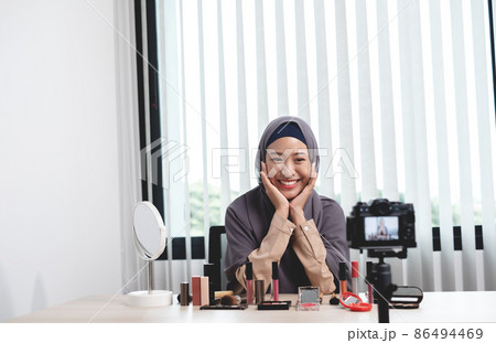 Muslim women making video beauty vlogger bloggers doing a cosmetic makeup tutorial vlog with brushes looking camera Save clips and share them on social media live via the internet Online 86494469