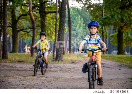 Two little kid boys in colorful casual clothes in summer forest park driving bicycle. Active children cycling on sunny fall day in nature. Safety, sports, leisure with kids concept Two little kid boys in colorful casual clothes in summer forest park driving bicycle. Active children cycling on sunny fall day in nature. Safety, sports, leisure with kids concept 86498668