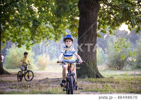 Two little kid boys in colorful casual clothes in summer forest park driving bicycle. Active children cycling on sunny fall day in nature. Safety, sports, leisure with kids concept Two little kid boys in colorful casual clothes in summer forest park driving bicycle. Active children cycling on sunny fall day in nature. Safety, sports, leisure with kids concept 86498670