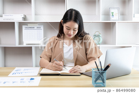 Asian woman taking notes in notebook while studying online in laptop at home, Video chat, Online communication , Stay home, New normal, Distance learning , Social distancing, Learn online. 86499080