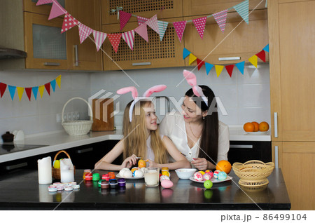 Mom and little daughter are sitting at the kitchen table and looking at each other while preparing for Easter. Mom and little daughter are sitting at the kitchen table and looking at each other while preparing for Easter. 86499104