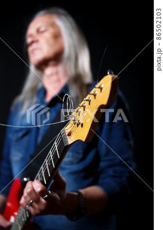 elderly man with long gray hair in blue denim shirt plays the electric guitar elderly man with long gray hair in blue denim shirt plays the electric guitar 86502103