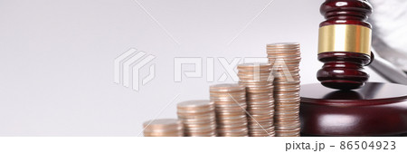 Judge wooden gavel lying near piles of coins in ascending order closeup Judge wooden gavel lying near piles of coins in ascending order closeup 86504923
