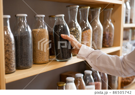 Woman in a store selling cereals by weight in an eco store. Trade concept without plastic packaging Woman in a store selling cereals by weight in an eco store. Trade concept without plastic packaging 86505742