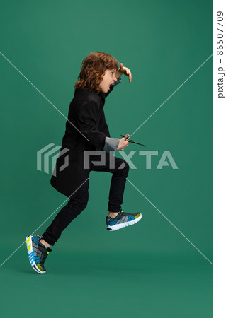 Full-length portrait of liitle boy, kid in image of stylish hairdresser, barber isolated on green studio background. Concept of occupation, modern specialists, childhood 86507709