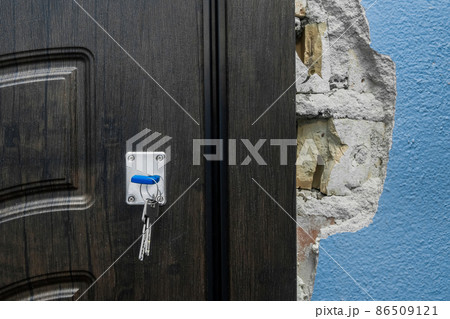 The keychain sits in the door lock as you open or close the entry or exit doors near an old broken wall in need of repair and reconstruction apartament, damaged architecture 86509121