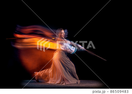 Portrait of beautiful woman in image of medieval warrior or knight with dirty wounded face with big sword isolated over dark background in mixed neon light. Portrait of beautiful woman in image of medieval warrior or knight with dirty wounded face with big sword isolated over dark background in mixed neon light. 86509483