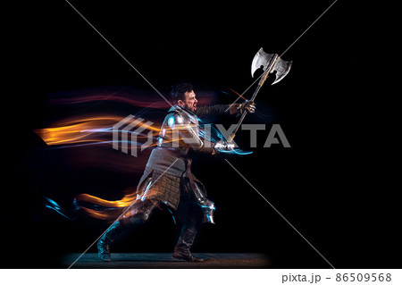 Dynamic portrait of brutal serious man, medieval knight with swinging ax fighting isolated over dark background in neon mixed light. Art, history, creativity 86509568