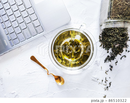 Office desk with glass cup of green tea and laptop Office desk with glass cup of green tea and laptop 86510322