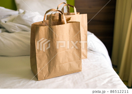 Delivery food craft bags on the bed on sunny day. Delivery in any weather around the clock to the client. Fast food eco packaging with big breakfast set Delivery food craft bags on the bed on sunny day. Delivery in any weather around the clock to the client. Fast food eco packaging with big breakfast set 86512211