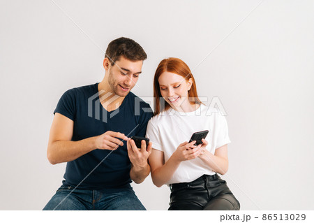Studio shot of young handsome man showing new mobile software app to smiling girlfriend on white isolated background. Happy black family couple sharing photos or contacts, using smartphones. Studio shot of young handsome man showing new mobile software app to smiling girlfriend on white isolated background. Happy black family couple sharing photos or contacts, using smartphones. 86513029
