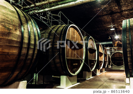Old barrels in the wine cellar. Wine cellar with old oak barrels, production of fortified dry or semi-sweet wine. The wine barrels are stored in the old cellar of the winery. Brewery, winery Old barrels in the wine cellar. Wine cellar with old oak barrels, production of fortified dry or semi-sweet wine. The wine barrels are stored in the old cellar of the winery. Brewery, winery 86513640