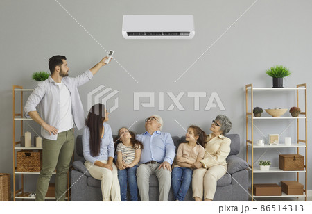 Happy family enjoying fresh air in cozy living room interior with new air conditioner at home. Young mother, kids and grandparents together relax on comfortable sofa under AC that father has turned on 86514313